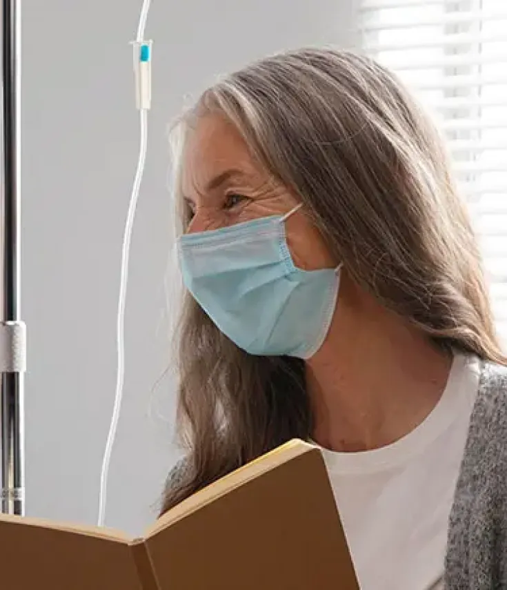 Sanitaria leyendo un libro a una paciente con pañuelo en la cabeza - Máster en Cuidados Paliativos UCAM