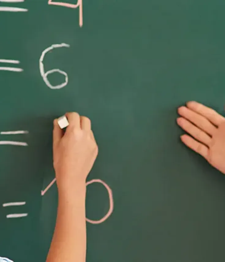 Niño de educación primaria resolviendo la tabla de multiplicar junto con su maestra graduada en Educación Primaria por UCAM Universidad.