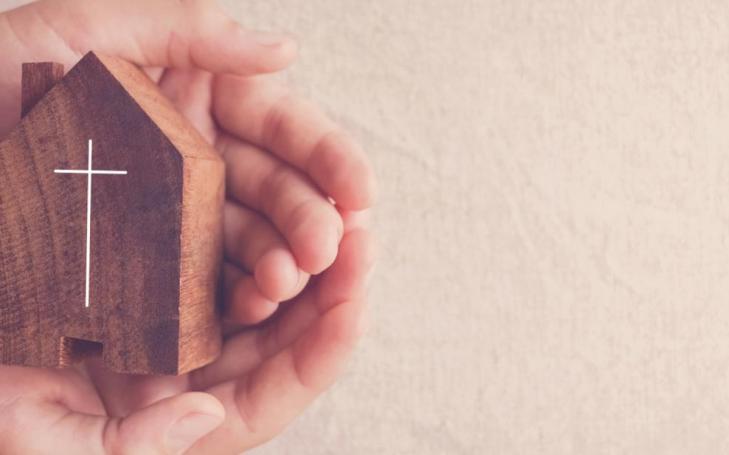 Manos sosteniendo una figura de casa con una cruz inscrita