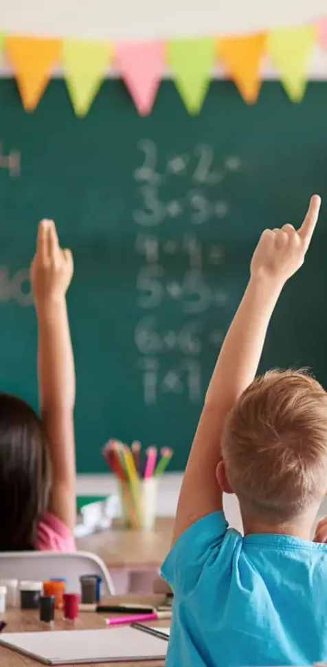 Niños levantando la mano en clase de matemáticas y dirigidos por su profesora graduada en el Grado en Educación Primaria de UCAM Universidad.