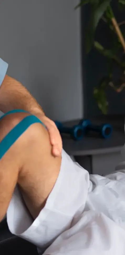Fisioterapeuta aplicando vendaje neuromuscular azul en la rodilla de un deportista en una sesión del Máster Universitario en Fisioterapia del Deporte en Madrid