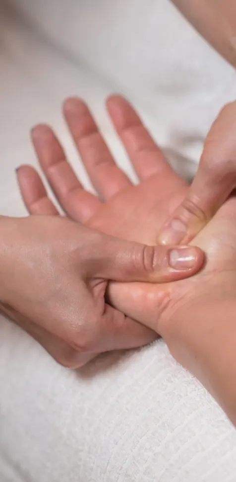 Primer plano de una terapeuta aplicando un masaje de reflexología terapéutica en la palma de la mano de un paciente en una camilla de prácticas en la UCAM.