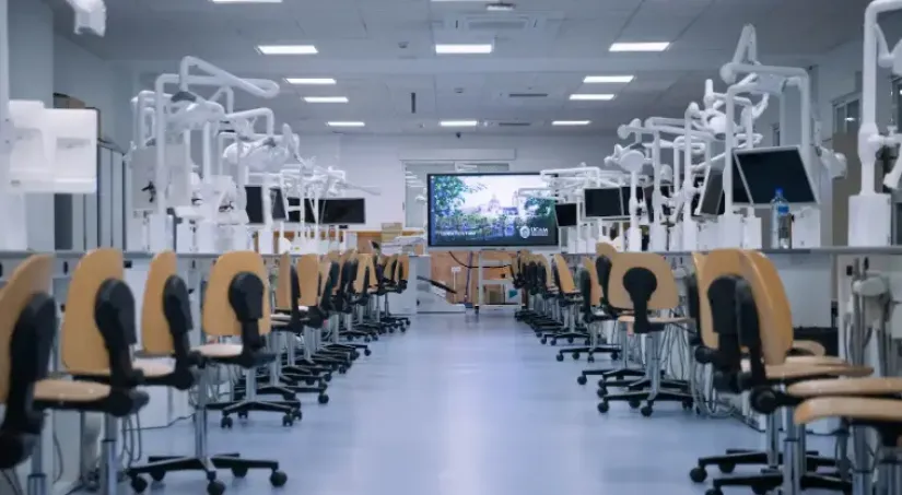 Preclínica Dental en UCAM con puestos equipados con instrumental rotatorio, maniquíes, lámparas LED y monitores para prácticas odontológicas y demostraciones del Grado en Odontología
