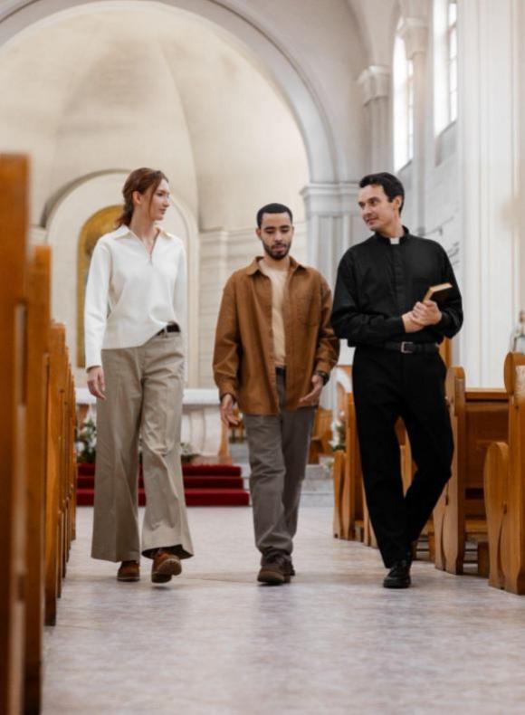 Sacerdote católico caminando y conversando con dos jóvenes en el interior de una iglesia