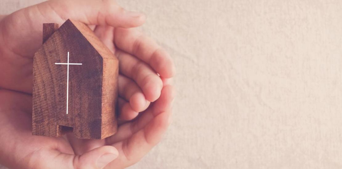 Manos sosteniendo una figura de casa con una cruz inscrita
