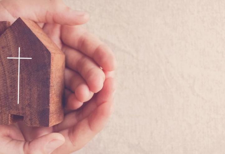 Manos sosteniendo una figura de casa con una cruz inscrita